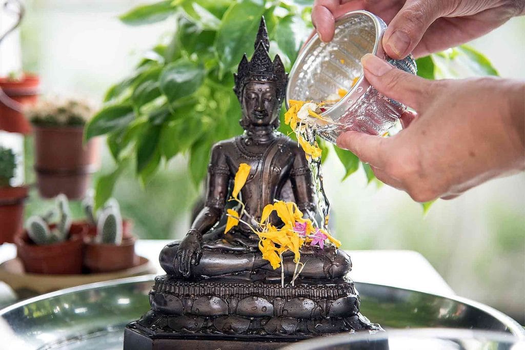 Traditional Songkran ritual: pouring fragrant water infused with Saraphi (Mammea siamensis) petals over Buddha statue for purification and renewal in Thailand